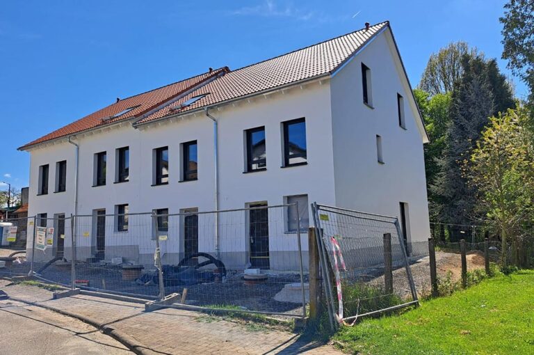 Modernes, weißes Reihenhaus im Bau, mit rotem Dach und blauem Himmel.