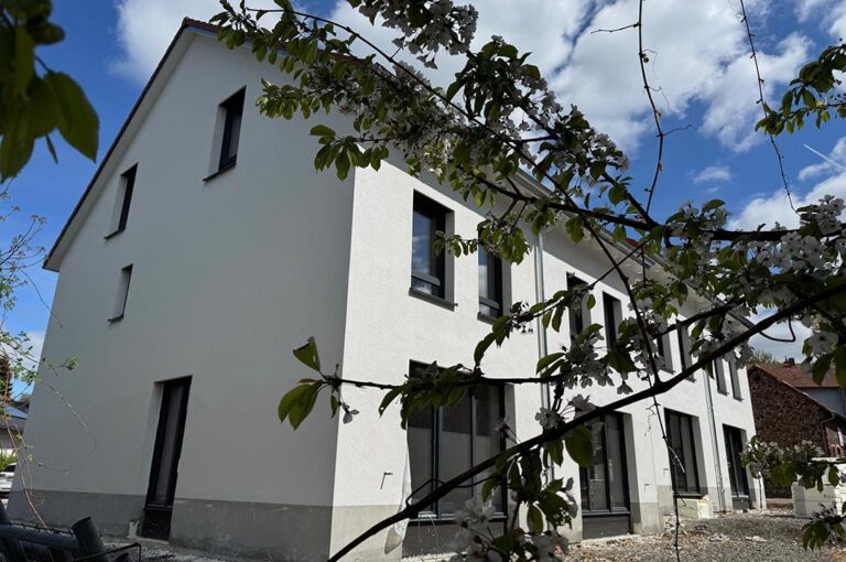Ein modernes, weißes Gebäude mit großen dunklen Fenstern unter blauem Himmel